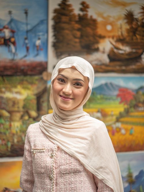 Free Portrait of a smiling woman wearing a hijab in front of vibrant artistic paintings. Stock Photo