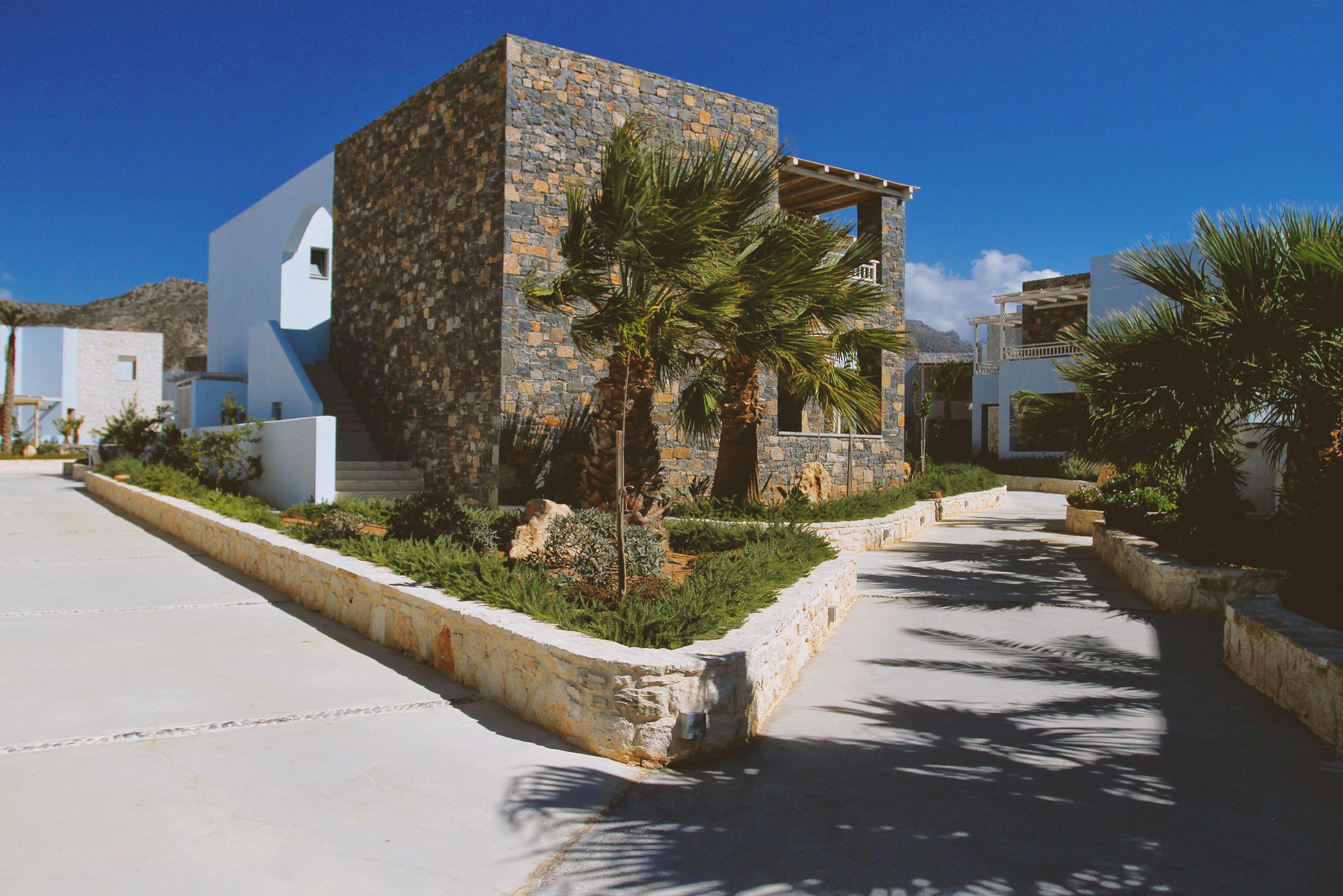 A beautifully designed stone villa amidst palm trees under a bright blue sky, exuding modern luxury.