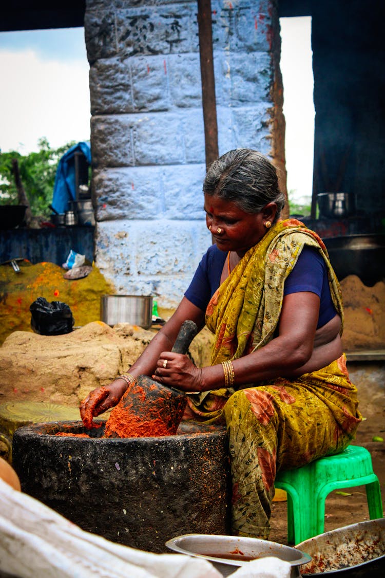 Indian Woman Powdering Spices In Big Stone Bowl