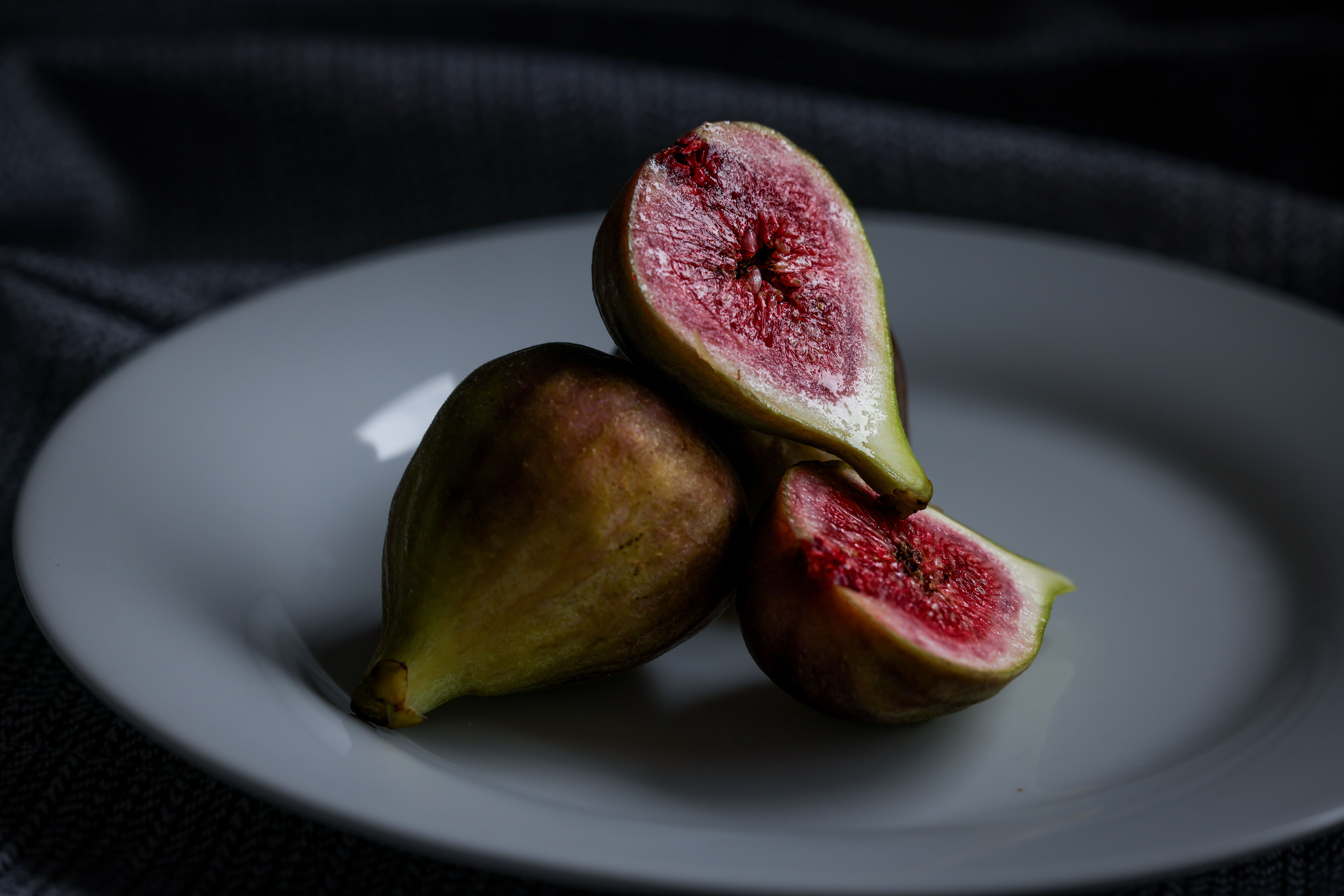 Fresh figs sliced open, displayed on a plate against a dark textured background.