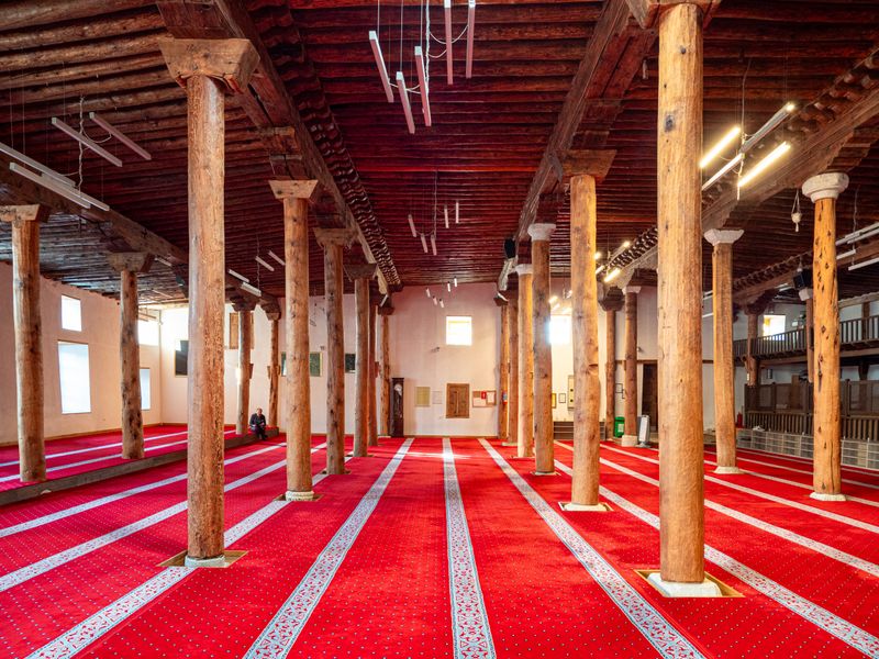 Mosque interior with wooden columns and vibrant red carpet