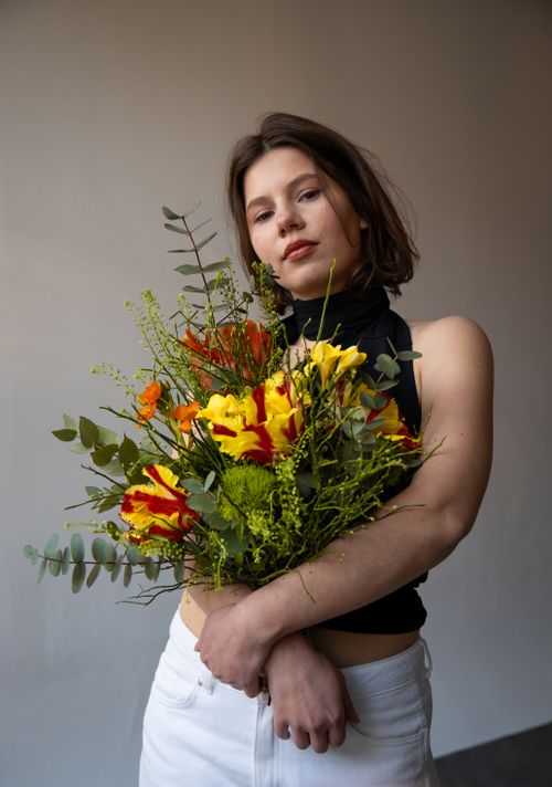 Free Young woman in black top holds vibrant bouquet indoors, posing serenely. Stock Photo