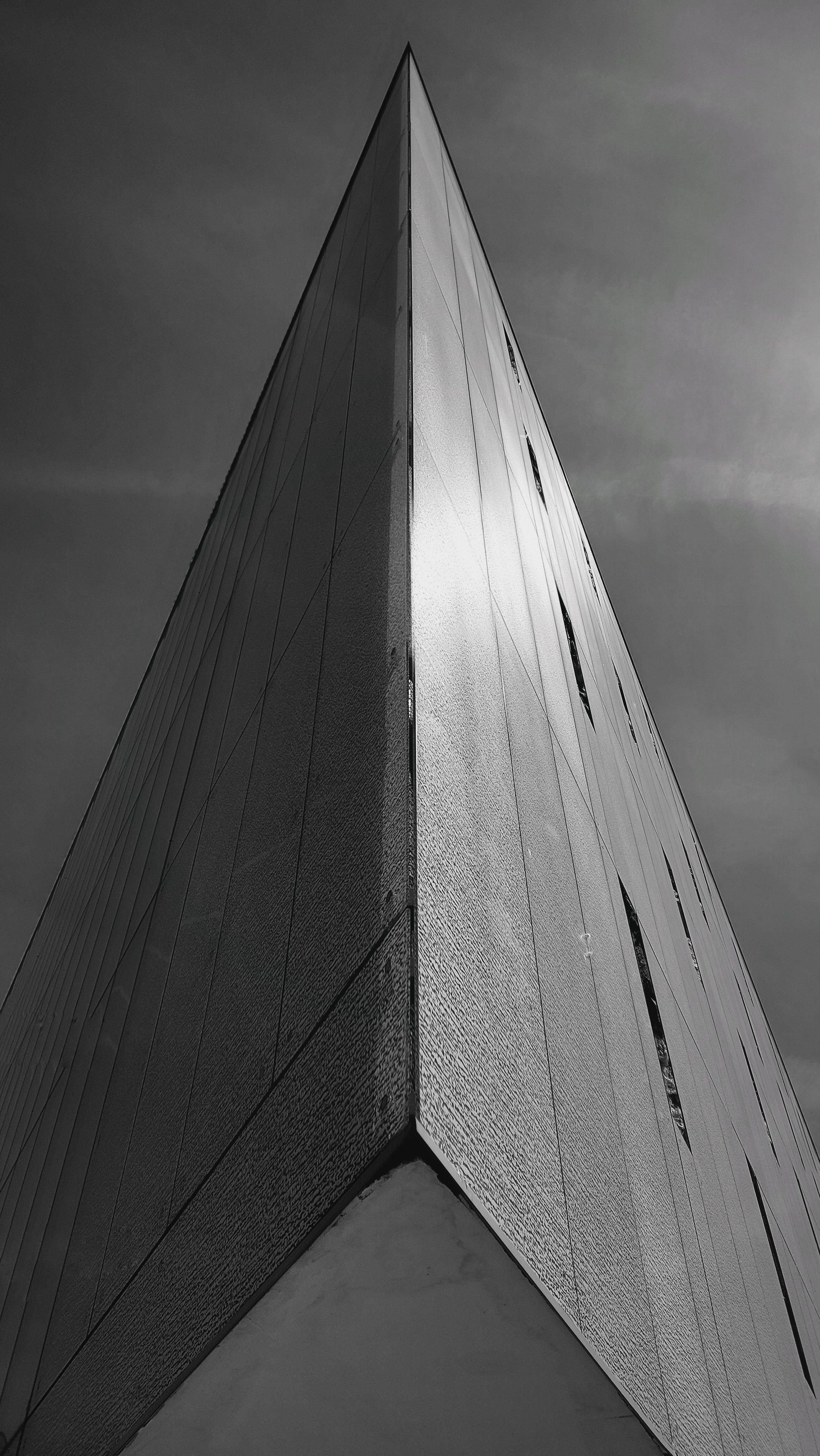 Dramatic black and white photo of a modern triangular building facade against a cloudy sky.