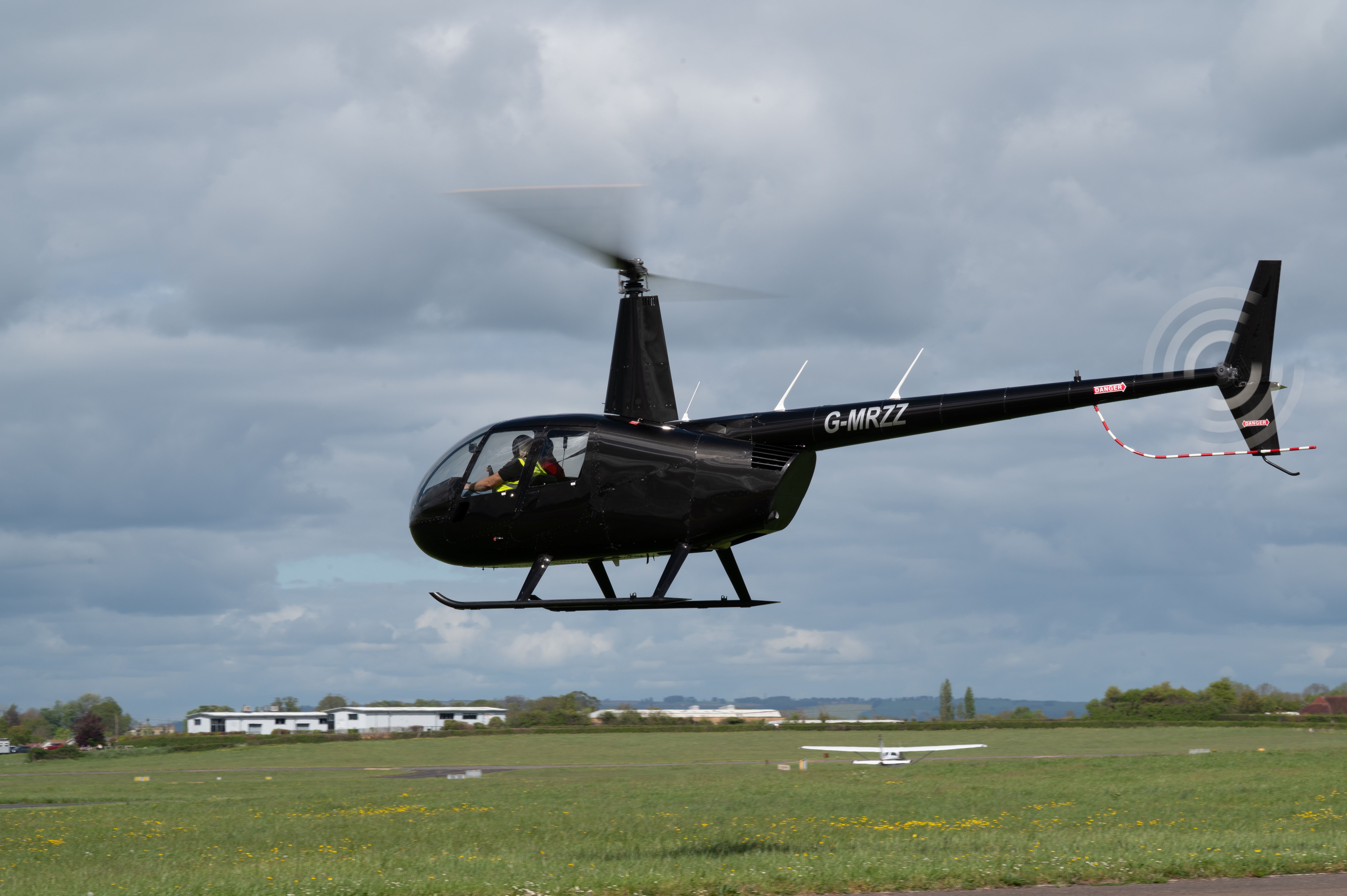 Robinson R44 Raven II helicopter flying at Staverton Airport on a cloudy day.