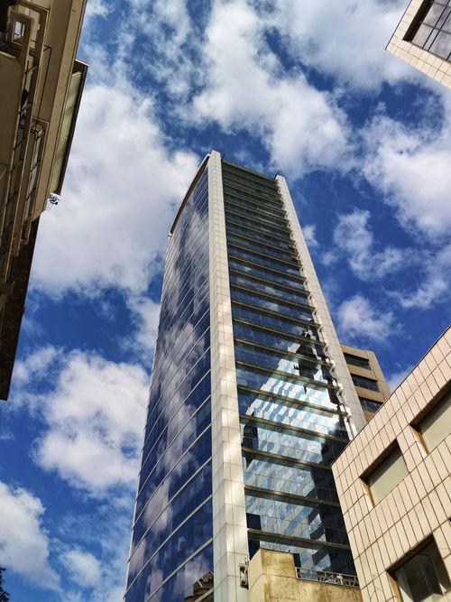Free A sleek modern skyscraper reflecting a vivid blue sky with clouds, capturing architectural elegance in an urban setting. Stock Photo