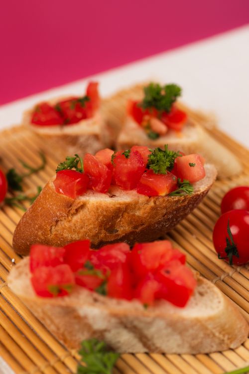 Free Delicious bruschetta topped with fresh tomato and garnish on a bamboo mat, perfect for appetizers. Stock Photo