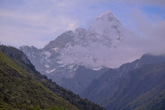 A breathtaking view of a snow-capped mountain with lush greenery and a cloudy sky.