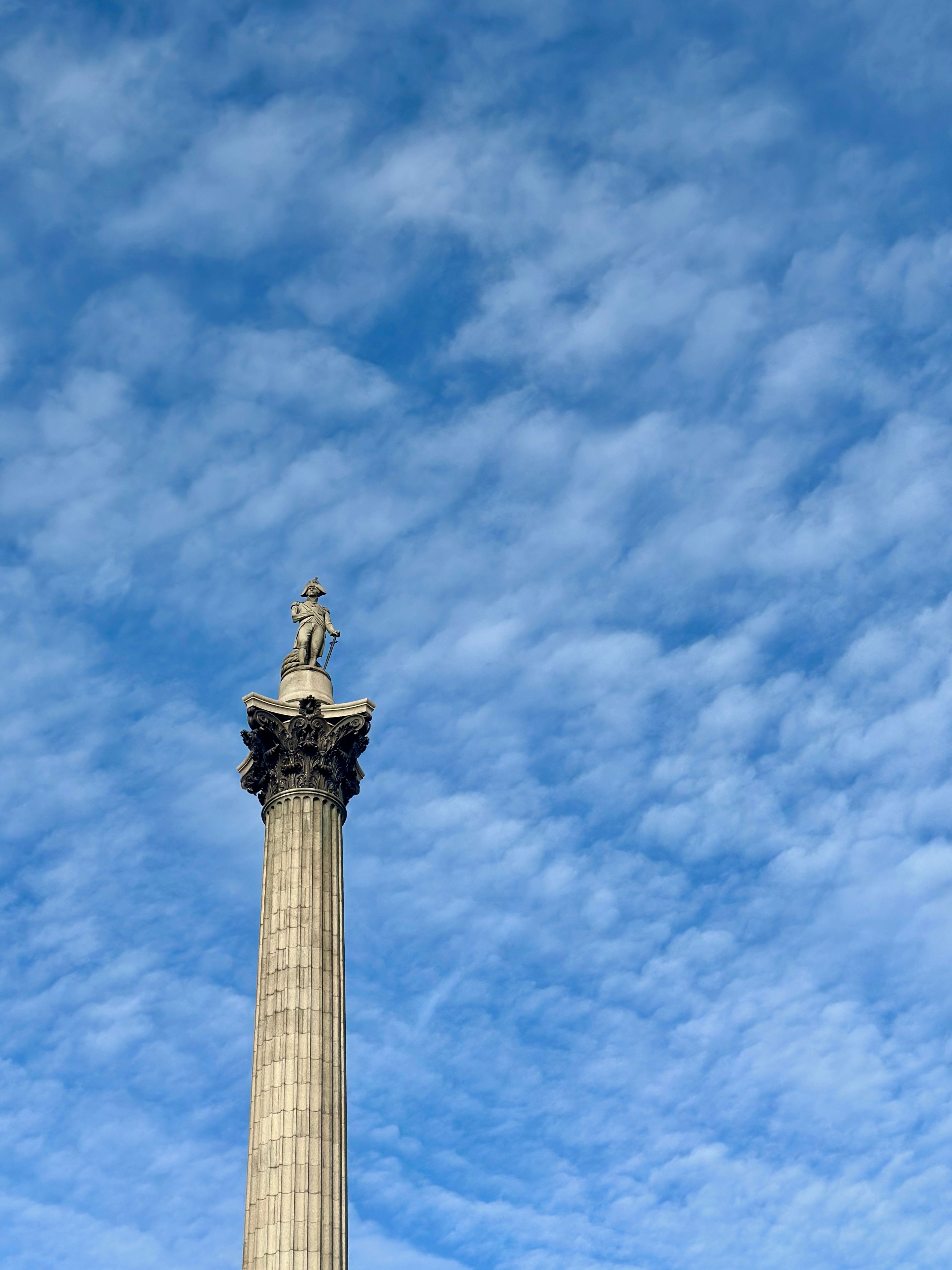 Nelson's Column in London stands majestically against a backdrop of a vivid blue sky with scattered clouds.
