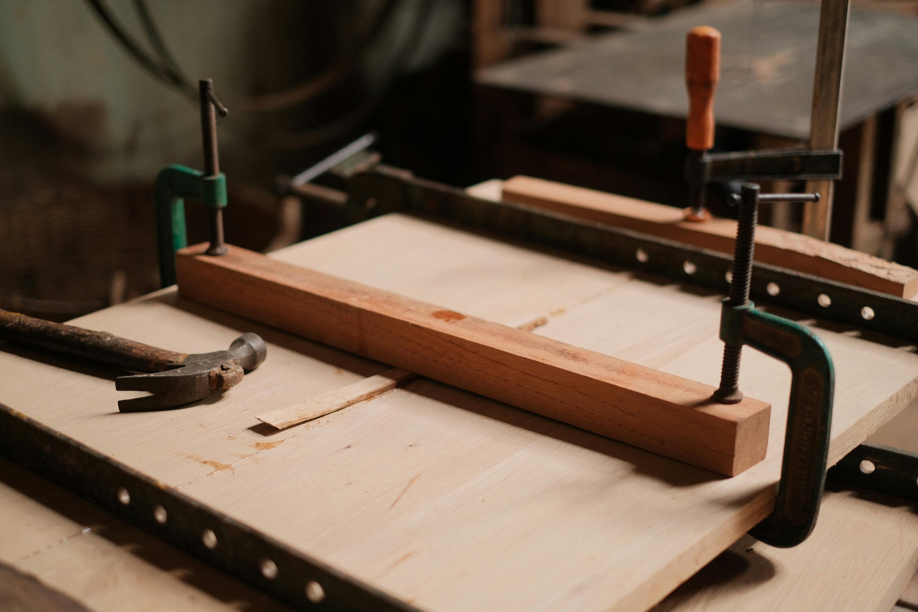 A woodworking workshop scene featuring clamps, a hammer, and wooden planks on a table.