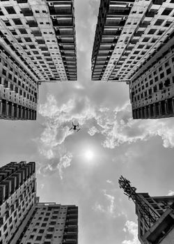 A dramatic view of tall buildings creating a frame around a sky with a drone flying high.
