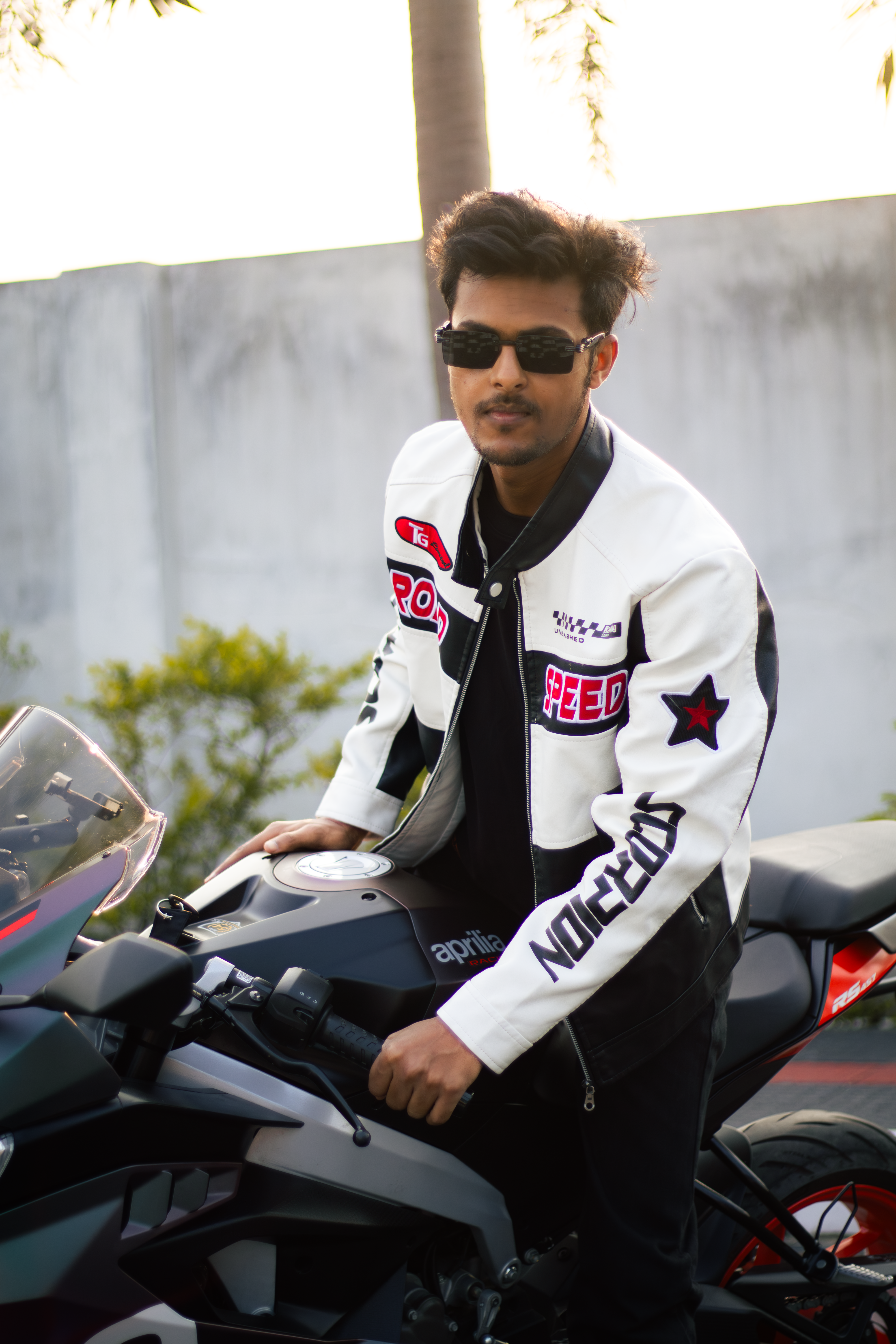 Confident man in stylish jacket poses with sleek motorcycle outdoors.