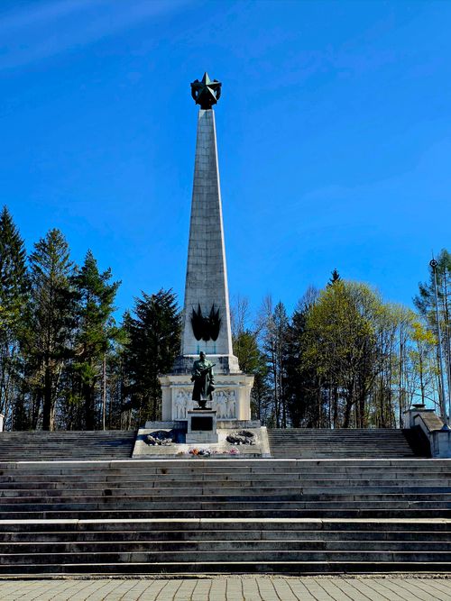 Free A towering obelisk monument under a clear blue sky surrounded by lush trees. Stock Photo