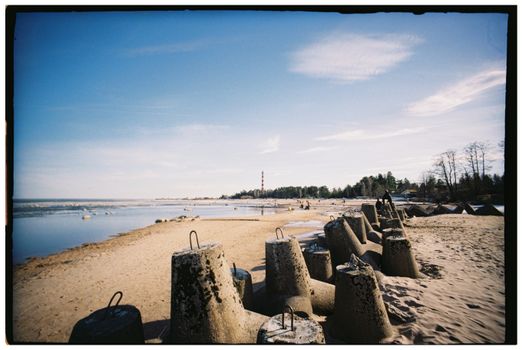 A serene coastal view with concrete blocks lining the sandy shore under a clear blue sky.