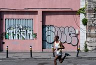 A marathon runner passes a graffiti-covered wall in an urban setting, showcasing street art.