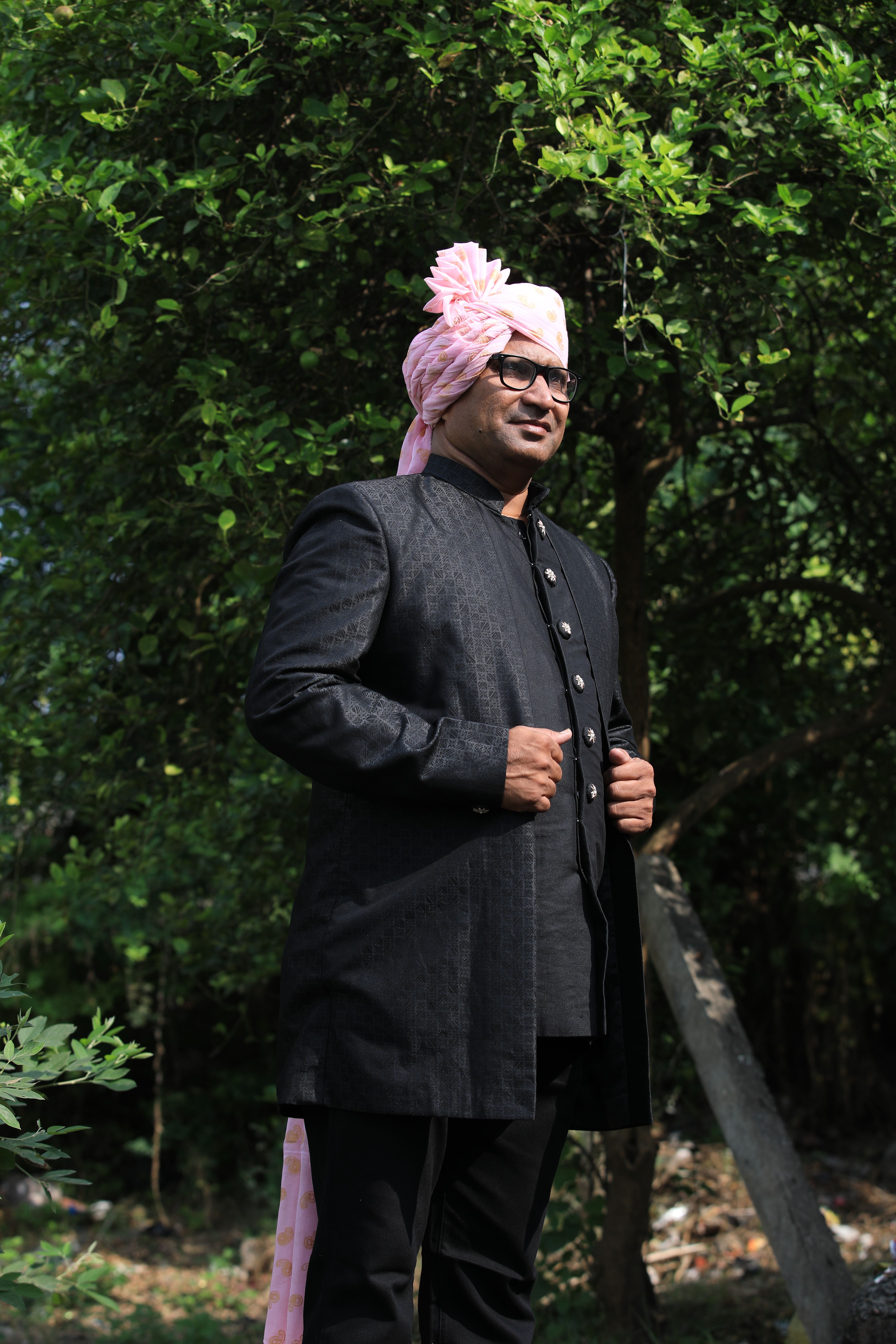 Man in traditional Indian wedding attire with pink turban posing outdoors.