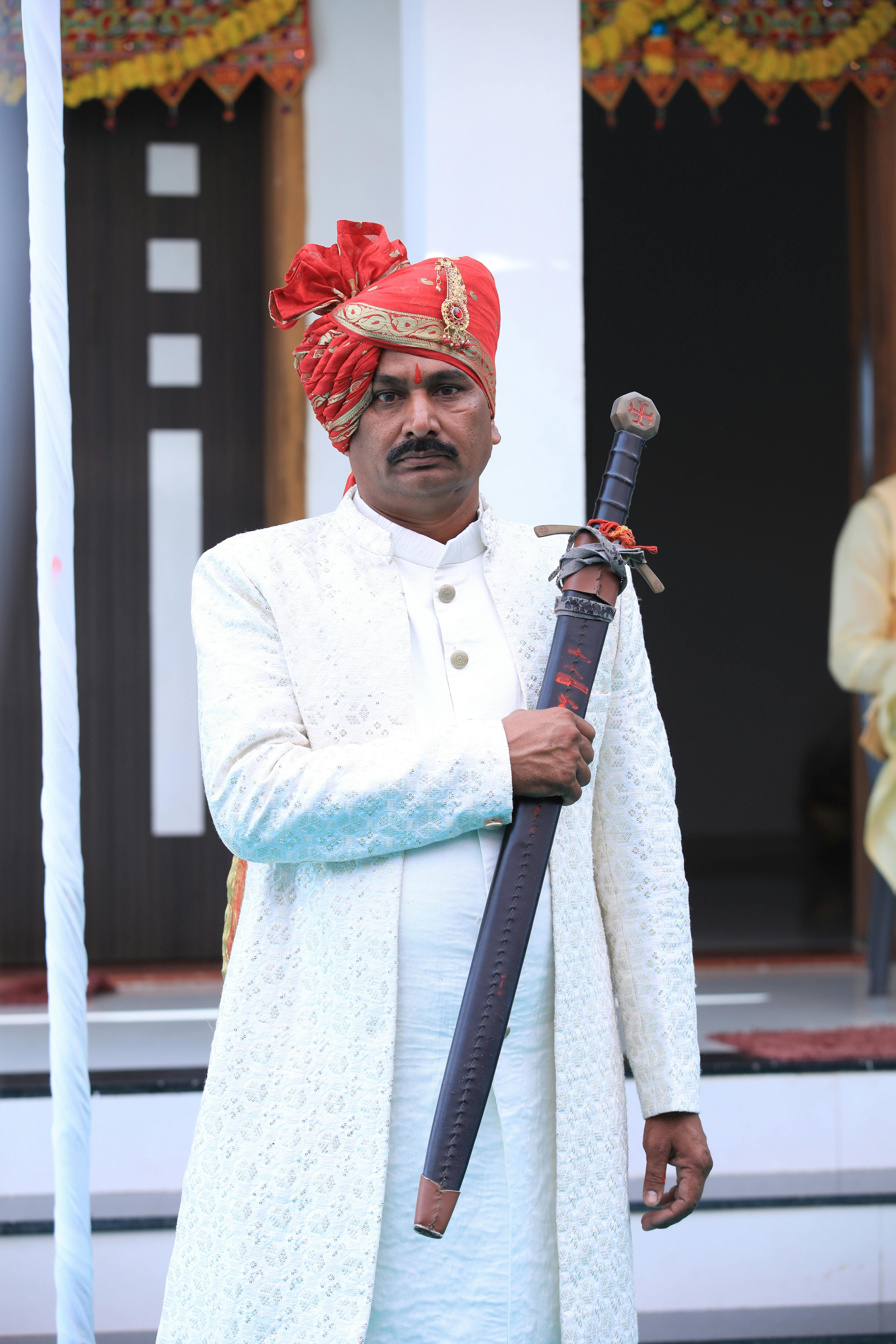 A traditional Indian groom wearing a sherwani and safa, holding a decorative sword.