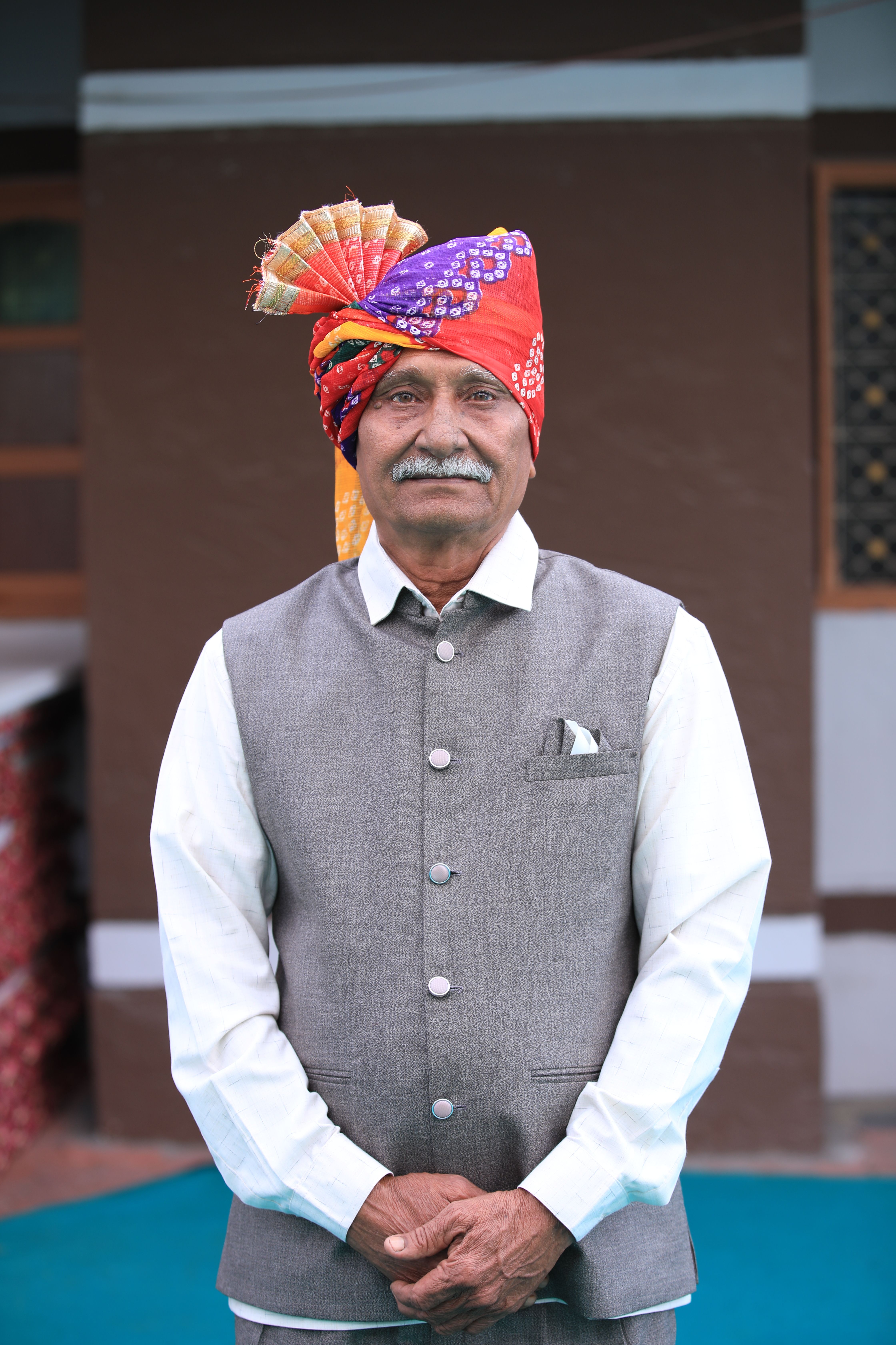 Elderly man wearing vibrant turban and traditional Indian attire, posing outdoors.