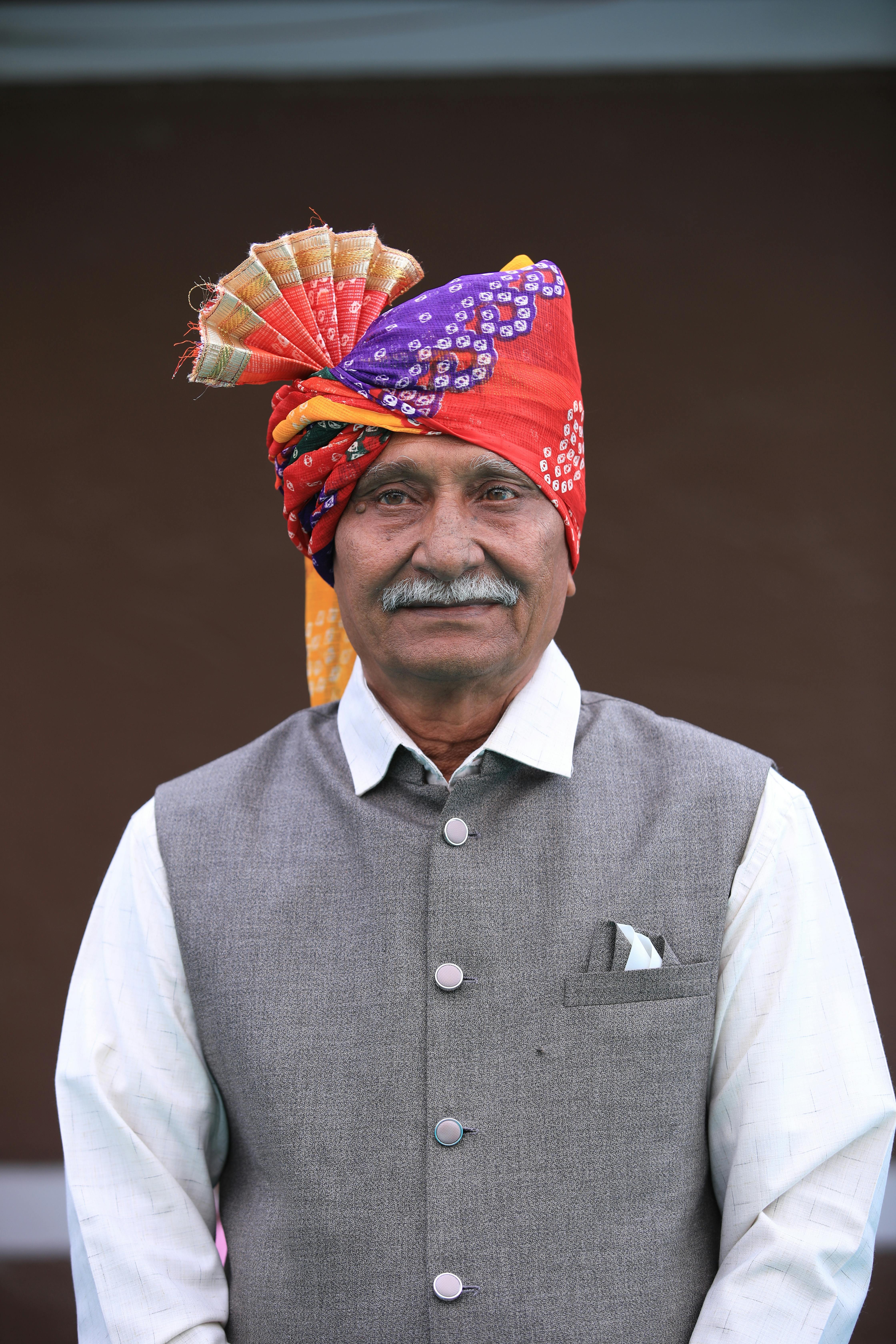 Elderly man in vibrant Indian turban and vest posing outdoors.