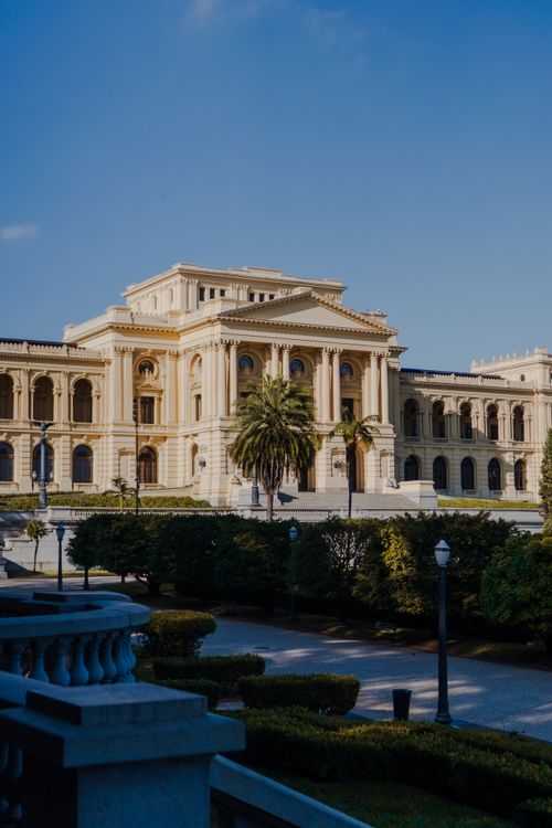 Free Stunning view of a historic neoclassical palace surrounded by lush gardens under a clear blue sky. Stock Photo