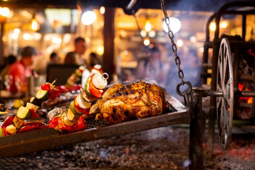 Sizzling roast meats and vibrant vegetables grilling over an open fire in a bustling market setup.