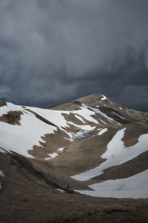 Free Dramatic mountains with partial snow coverage beneath an ominous cloudy sky, capturing the beauty of nature. Stock Photo