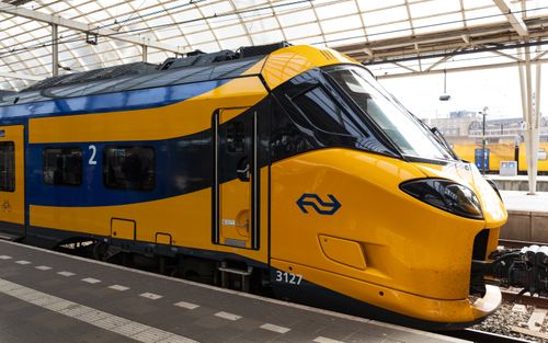 Free A modern yellow and blue train at an Amsterdam station platform under a glass roof. Stock Photo