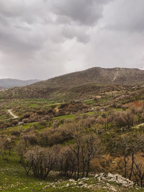 Free Panoramic view of a mountainous landscape in early spring with a cloudy sky, showcasing vibrant greenery and path trails. Stock Photo