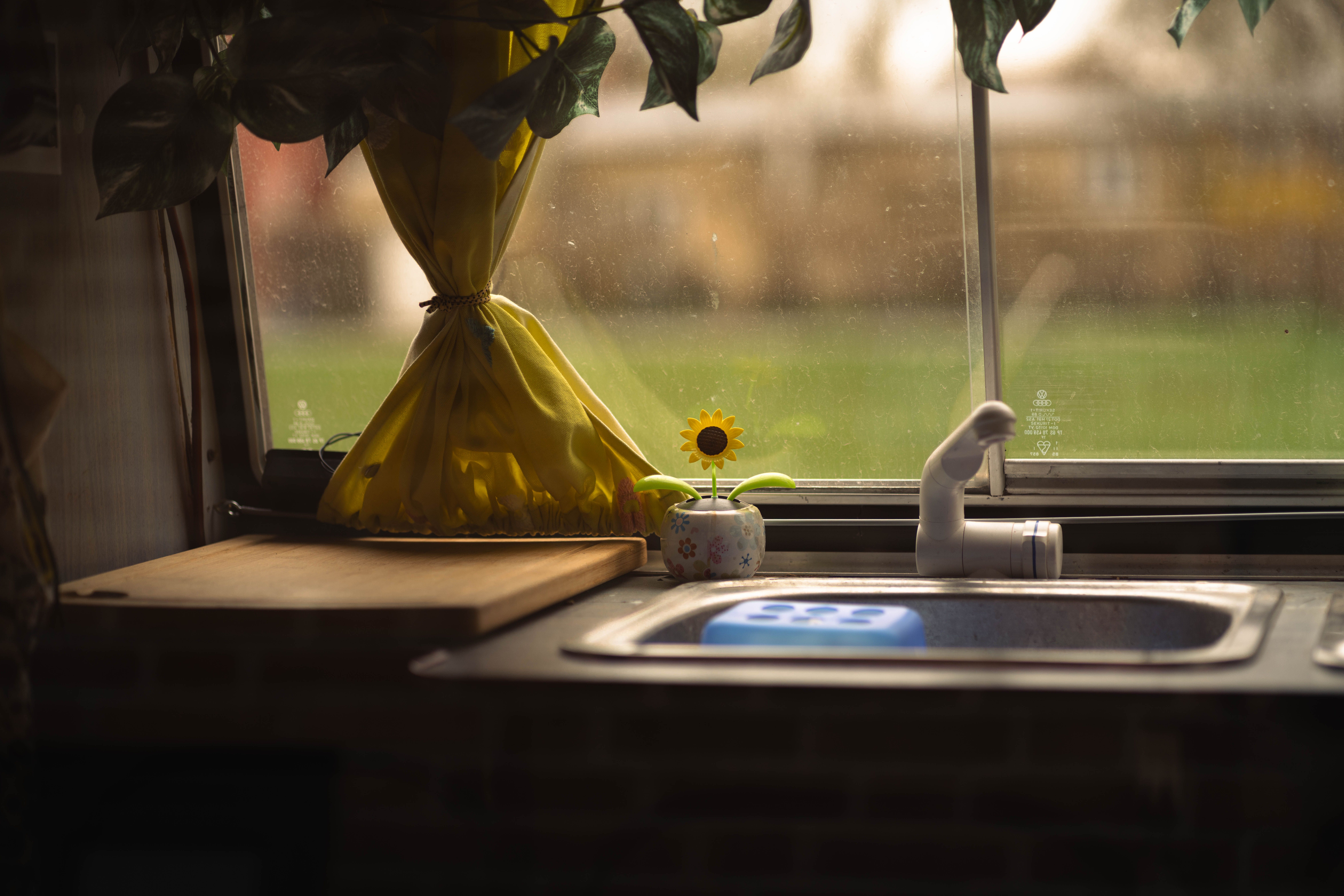 Warm and inviting kitchen sink scene with a sunflower decoration and yellow curtains overlooking a green field.
