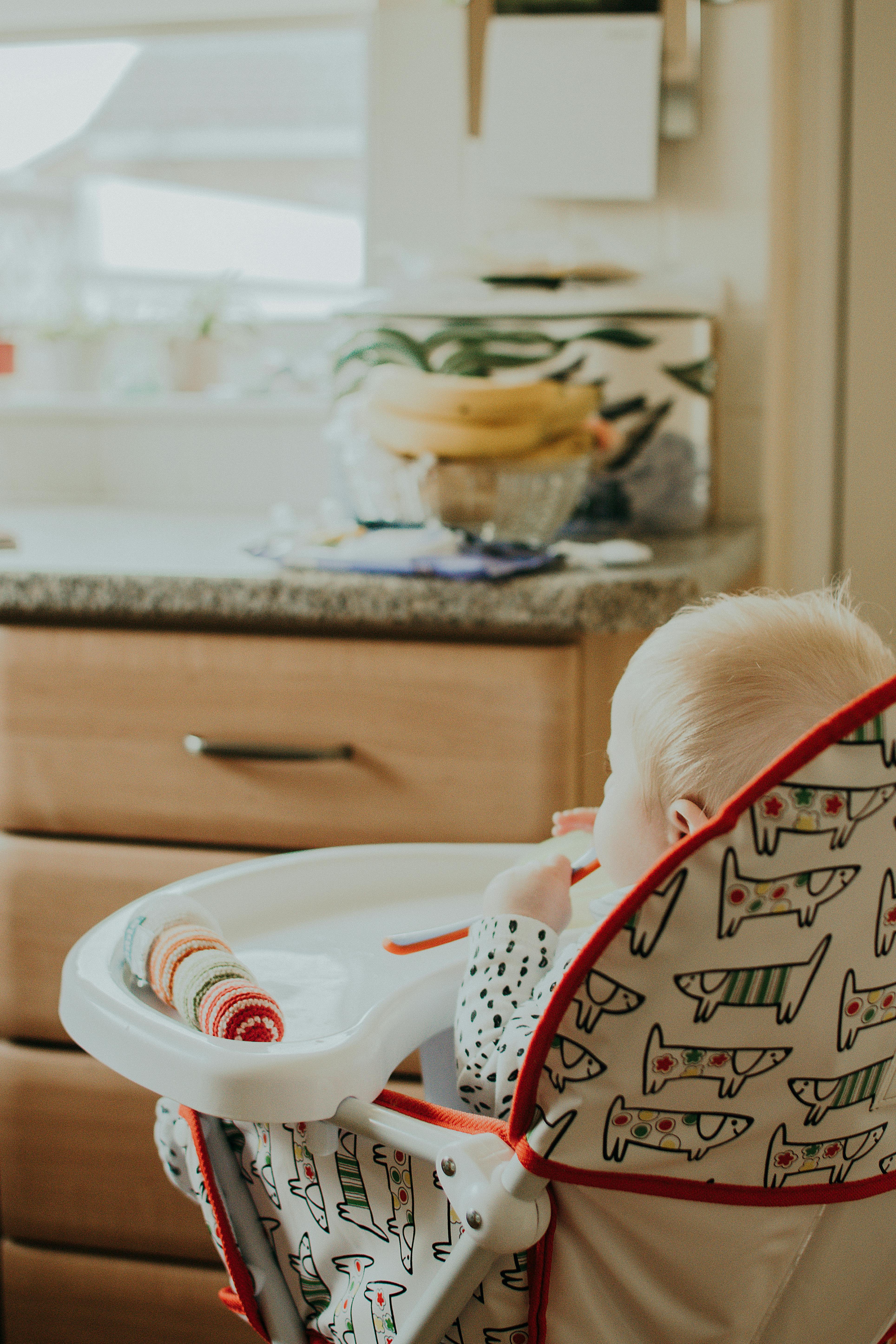 一个可爱的宝宝正坐在厨房里舒适的彩色高脚椅上享用美食