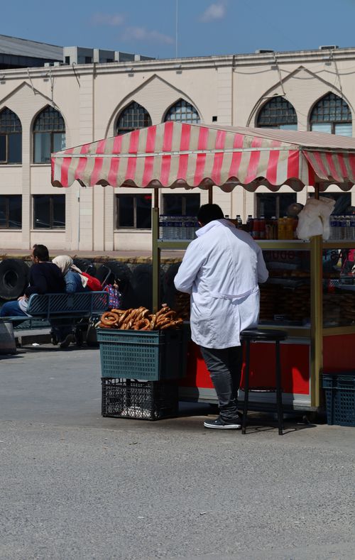 Free A street vendor selling pretzels from a cart under a striped canopy in a vibrant outdoor setting. Stock Photo