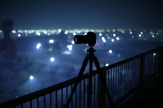 Silhouette of a camera on a tripod capturing city lights at night.