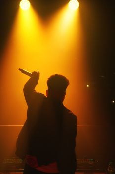 Dynamic silhouette of a male singer performing under warm stage lights.