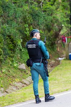 A Guardia Civil officer monitoring a roadside area with greenery in the background.