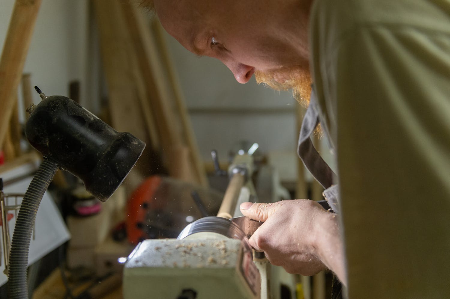 Artisan skillfully shapes wood on a lathe under focused workshop lighting