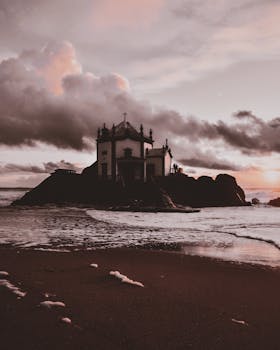 岩石海岸上，一座教堂映衬着戏剧性的日落，海浪与鲜艳的天空色彩被捕捉其中
