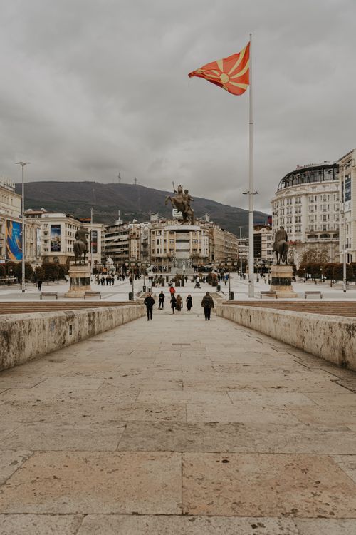 Free View of Macedonia Square in Skopje featuring the Skanderbeg Monument and Macedonian flag under a cloudy sky. Stock Photo