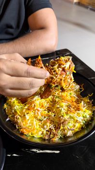 A person enjoying a flavorful plate of biryani with their hand in a casual dining setting.