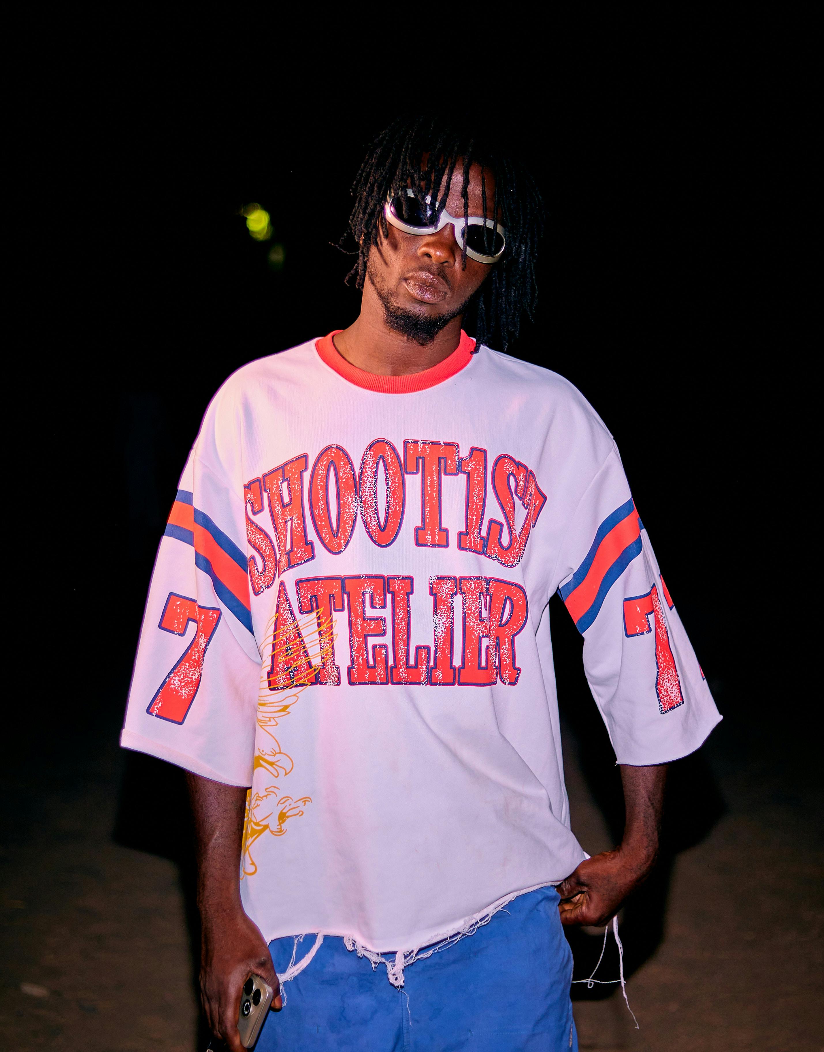 A fashionable young man poses confidently in a colorful outfit, showcasing urban street style at night.