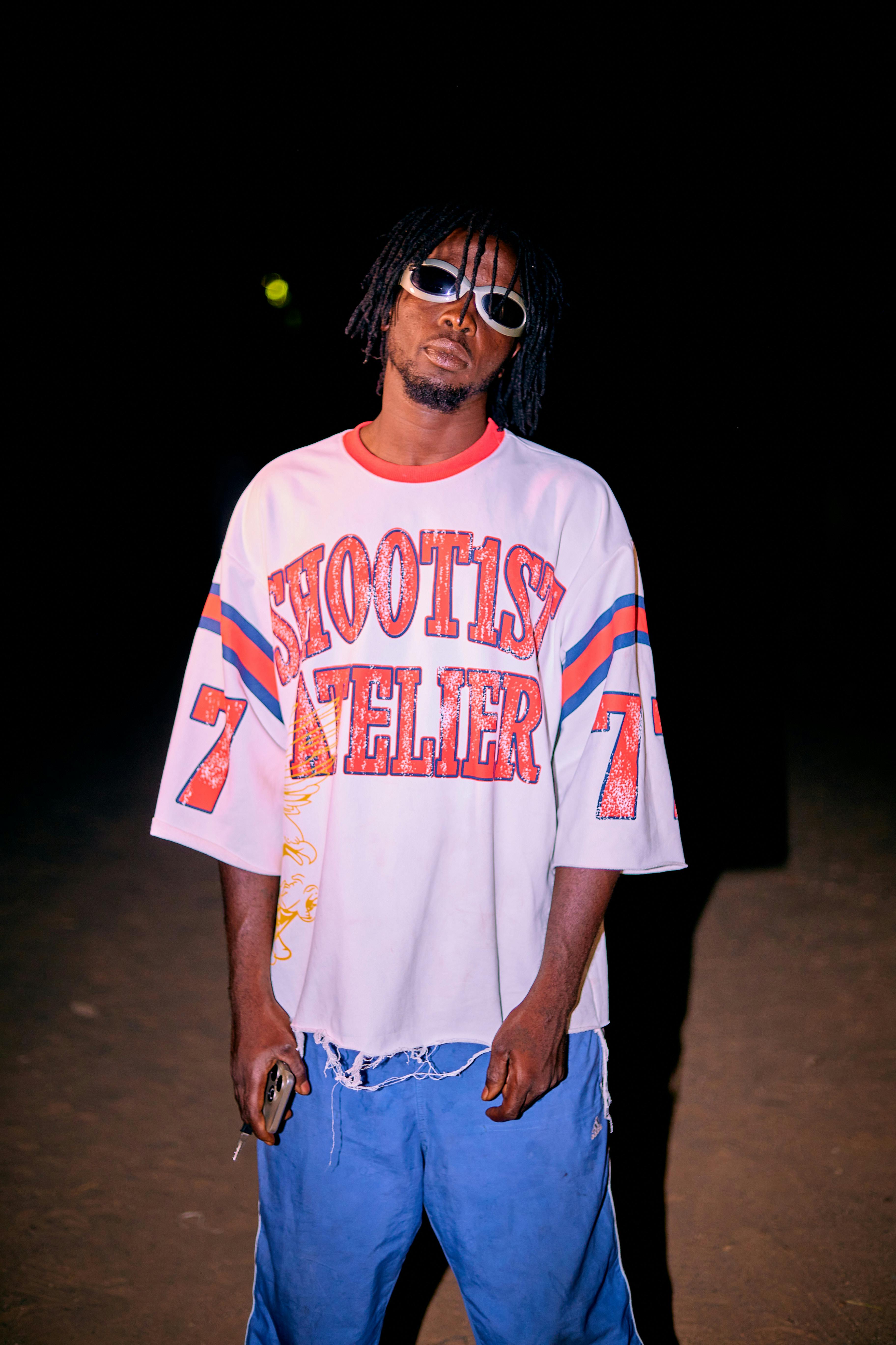 Stylish individual in sunglasses and graphic tee standing outside at night.