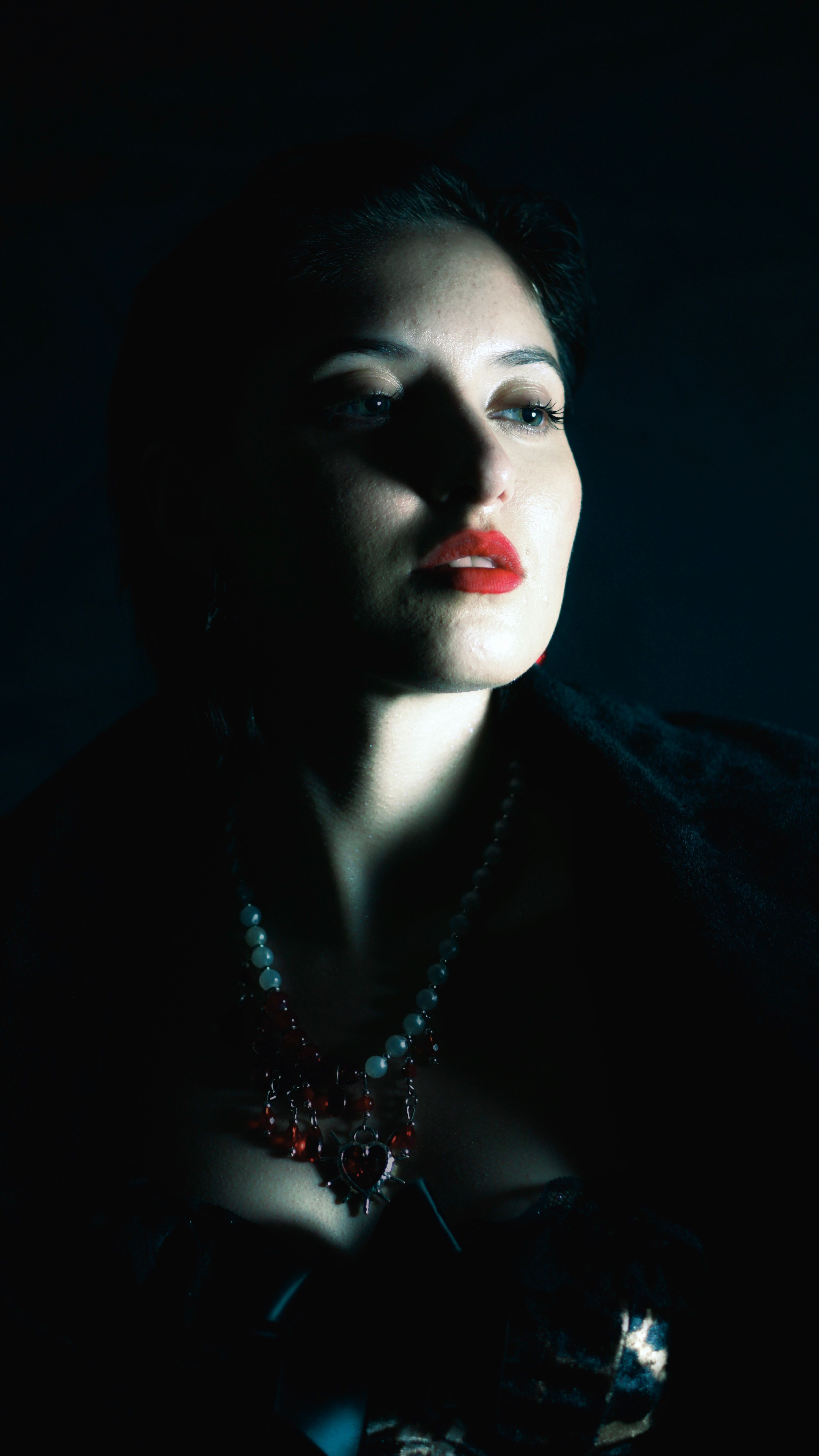 Dramatic chiaroscuro portrait of an elegant woman with bold red lips gazing away into the shadows