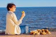 A woman enjoys empanadas by the ocean in Montevideo, Uruguay during a sunny day.