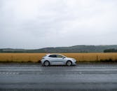 天空多云，一辆银色汽车停在潮湿的路边，旁边是一片干草田