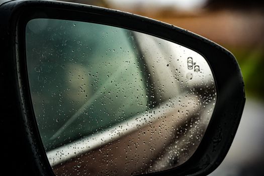 Close-up of a car side mirror with raindrops, reflecting a blurred background.