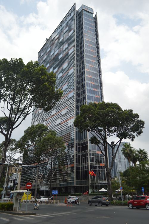 Free Tall modern skyscraper surrounded by lush trees in a bustling city setting. Stock Photo