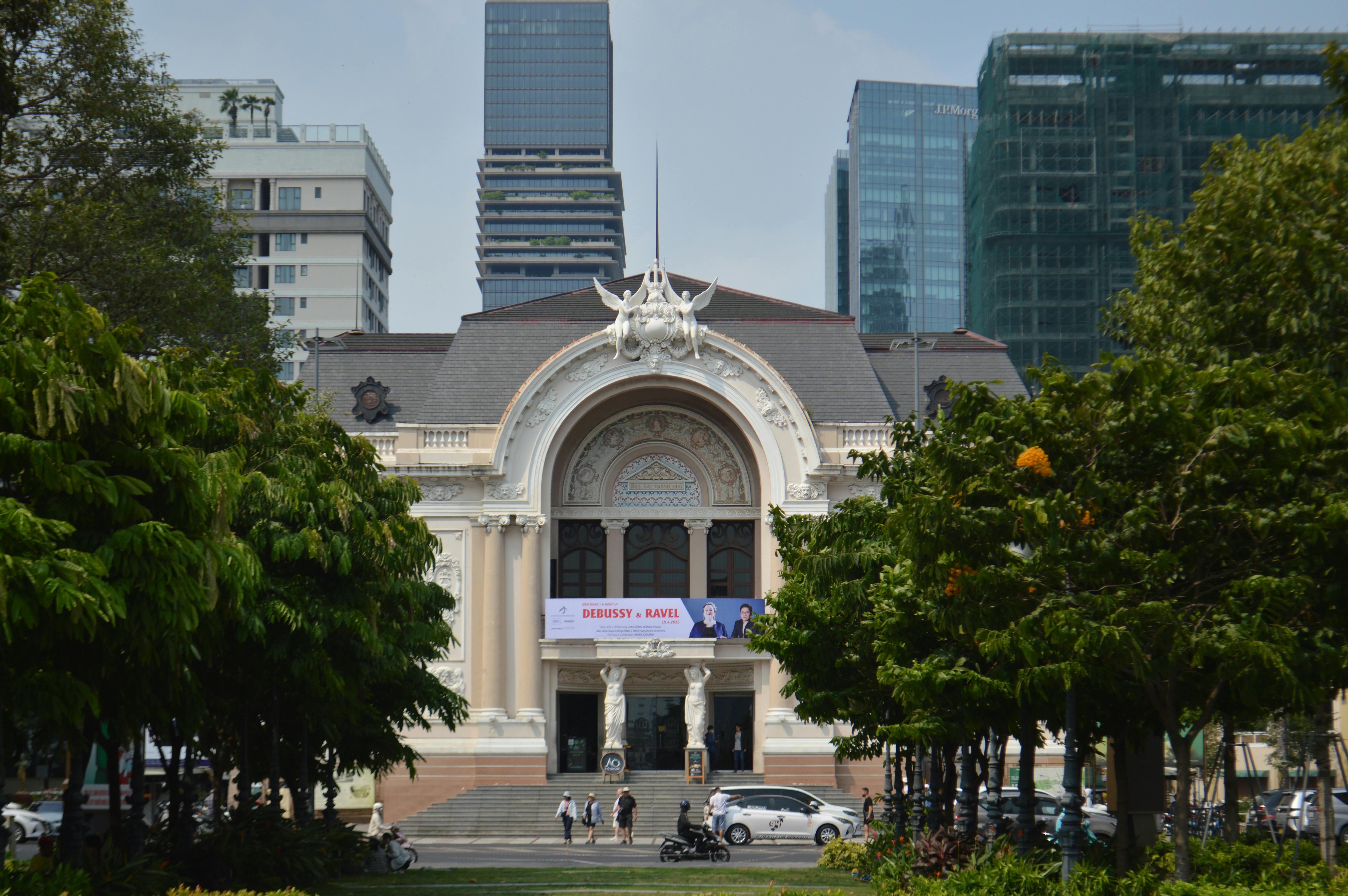 Saigon Opera House with modern buildings, trees, and people in daylight.