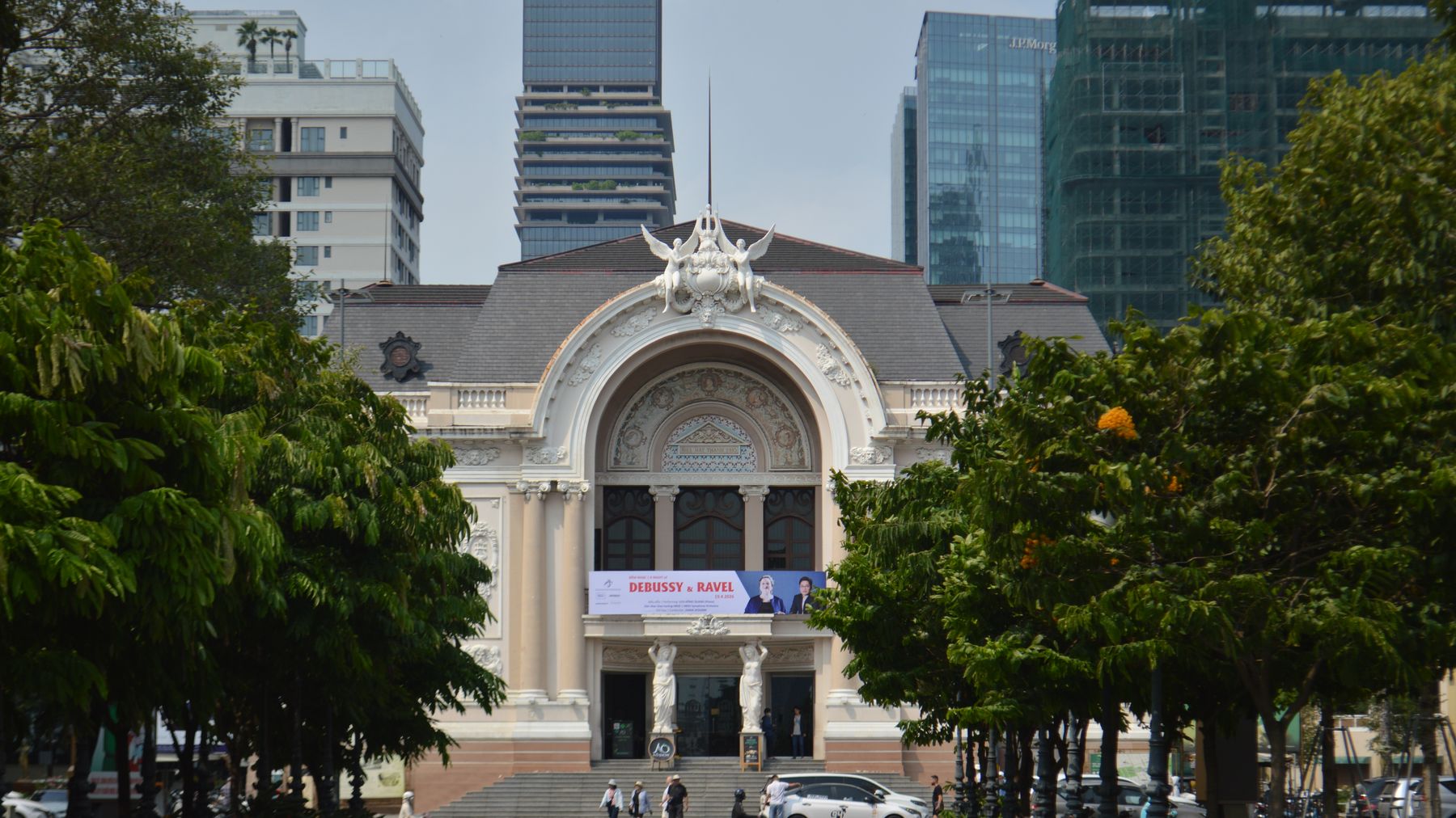Saigon Opera House with modern buildings, trees, and people in daylight.