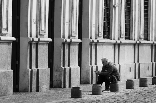 Free A man sitting on a sidewalk curb in front of historic buildings in Santiago de Chile. Stock Photo