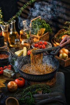 A steamy bowl of spaghetti with tomatoes and herbs in a rustic kitchen setting.