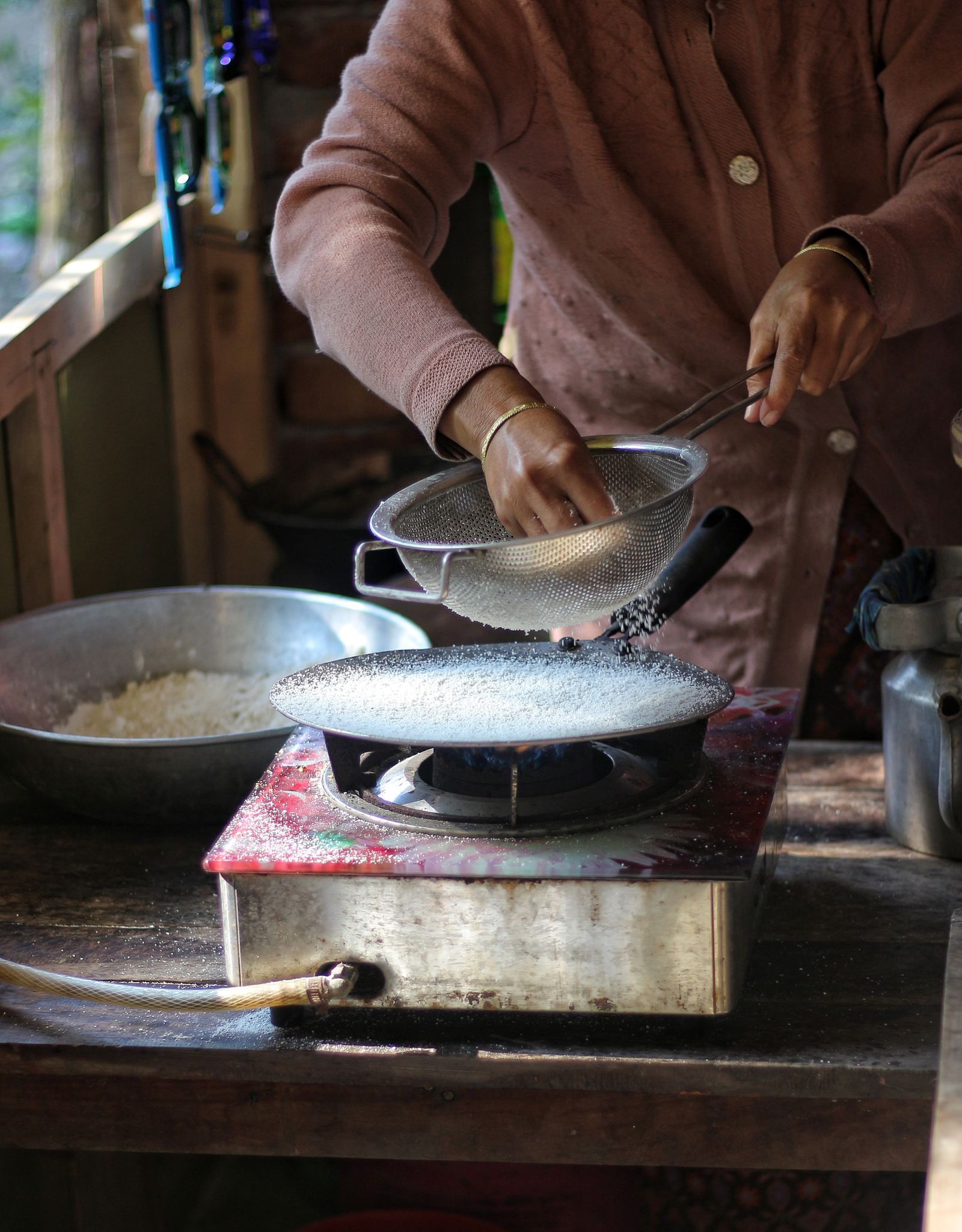 Woman preparing traditional rice dish over a gas stove in rustic setting, showcasing cultural cooking methods.
