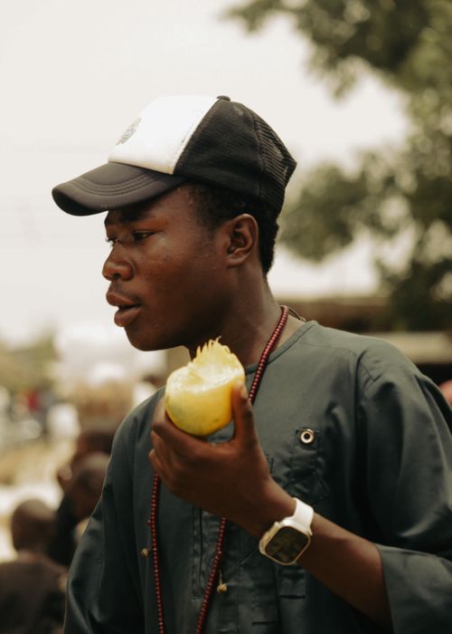 Free A young man wearing a cap and smartwatch enjoys a fresh mango outdoors. Stock Photo
